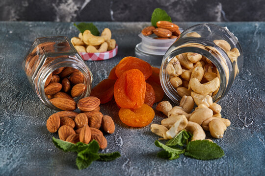 Cashew almonds spill out of transparent cans, dried apricots lie between them against the background with a blue tint.