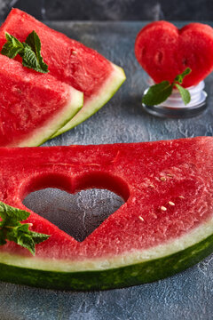 Composition with ripe watermelon, mint leaves and a heart carved in a slice of watermelon, on a background with a blue tint. Concept for valentines day