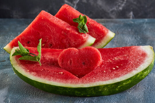 Composition with ripe watermelon, mint leaves and a heart carved in a slice of watermelon, on a background with a blue tint. Concept for valentines day