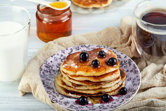 Tasty breakfast. A stack of pancakes with honey syrup a glass of milk, espresso coffee and honey on a wooden white background