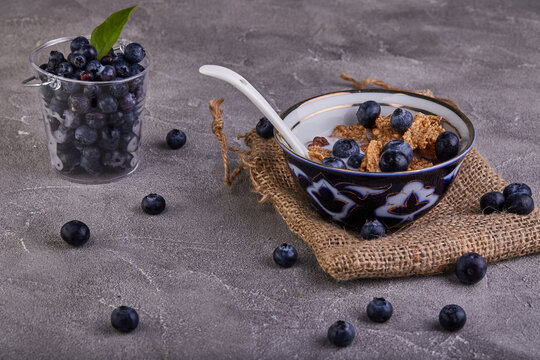 Fresh blueberries and a bowl with cornflakes and milk on a gray concrete background