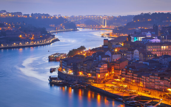 Porto, Portugal. Evening sunset panoramic view at nighttime town and Ponte de Dom Luis bridge with tramways. Coastline of river Douro with reflections of illumination in water and picturesque clouds.