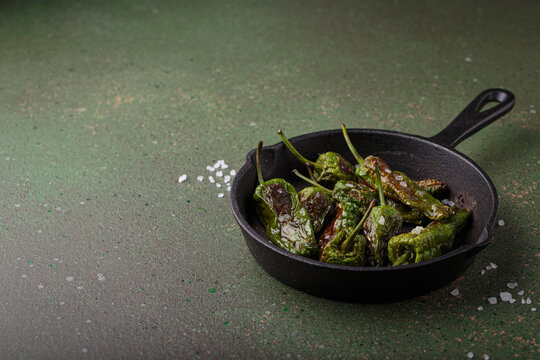 Padron peppers fried cast iron skillet sea salt dark green background Spanish appetizer copy space