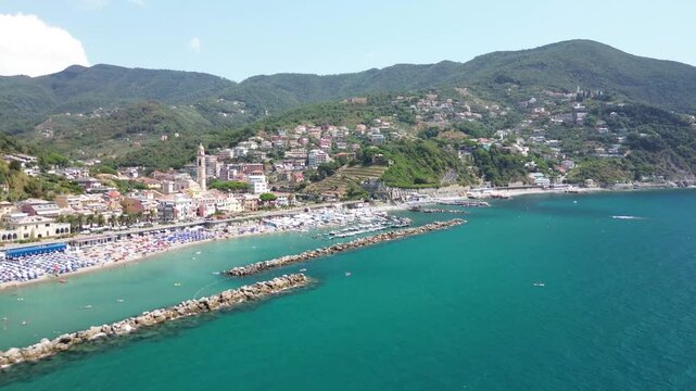 Moneglia, Liguria, Italy. Lateral aerial drone flight along Moneglia Beach, stone breakwaters and turquoise Ligurian Sea, revealing the seaside town on the Riviera di Levante.