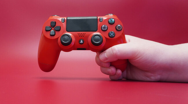 Red DualShock 4 gamepad in hand on a red background. PS4 controller, close-up, studio shooting.