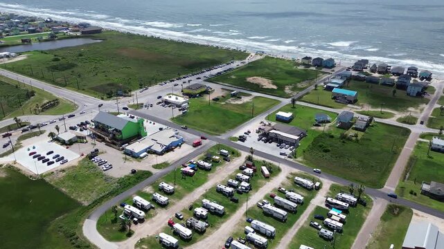 Orderly vacation trailers border Fort Velasco Drive leading toward Bluewater Highway parking zones. Colorful stilt residences line surging coastal tides across Surfside Beach, Texas