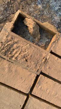 Close-up of a worker manually shaping wet clay inside a rectangular mold during a traditional handmade brick production process.