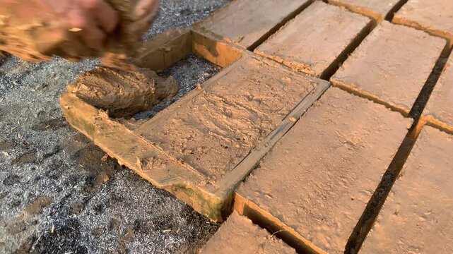 Close-up of a worker manually shaping wet clay inside a rectangular mold during the traditional production of handmade clay bricks.