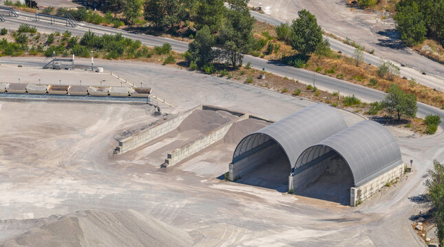 Aerial view of covered aggregate storage structures, gravel stockpiles and material bays at an industrial quarry and construction materials facility in Valence, Auvergne-Rhone-Alpes, France.