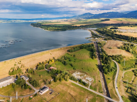 Aerial view of Liptovska Mara hydroelectric plant with its large reservoir, surrounding green fields, and distant mountains in Liptovsky Mikulas District, Zilina Region, Slovakia.