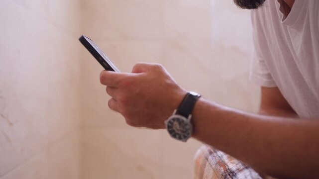 Middle-aged man looking at smartphone while sitting on toilet during a private moment, engaging in masturbation and self-stimulation, illustrating adult lifestyle, privacy and modern digital habits.