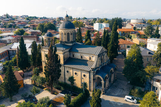 Aerial view of the historic Bagrati Cathedral surrounded by lush trees and urban rooftops in Kutaisi, Imereti, Georgia.