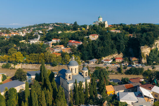 Aerial view of the historic city of Kutaisi featuring the Bagrati Cathedral on the hill and a church in the foreground, surrounded by trees and architecture in Kutaisi, Imereti, Georgia.