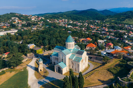 Aerial view of Bagrati Cathedral with its distinctive green roof, surrounded by lush trees and the urban landscape of Kutaisi, Imereti, Georgia.