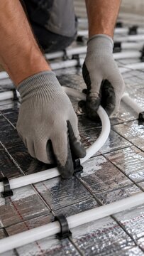Man installing underfloor heating pipe on reflective insulation foil. Worker laying radiant warm floor tubing with fixing clip. Modern hydronic heating technology and home construction concept