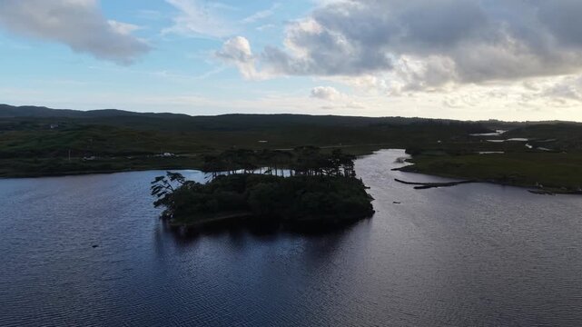 Aerial drone footage flying around Pine Island in Derry Lough, County Galway, Ireland. The footage shows a small wooded island surrounded by dark freshwater, rocky shores and scenic Connemara