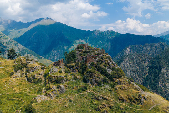 Aerial view of the historic Diklo fortress ruins on a rocky mountain ridge, surrounded by green slopes and the towering peaks of the Caucasus Mountains in Diklo, Kakheti, Georgia.