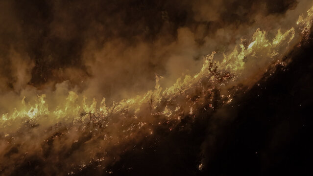 Aerial view of a wildfire burning on the slopes of Table Mountain with intense flames and thick smoke rising into the night sky in Cape Town, Western Cape, South Africa.