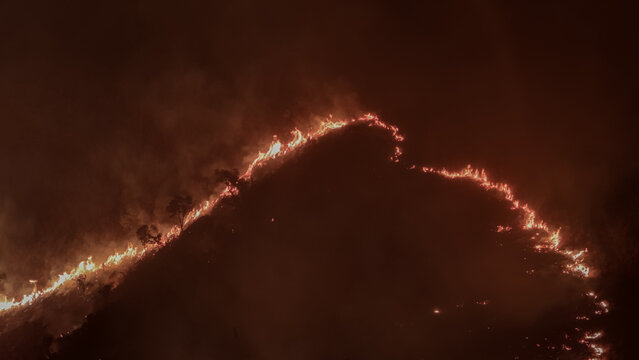 Aerial view of a wildfire burning along the ridge of Table Mountain at night with glowing flames and smoke rising into the dark sky in Cape Town, Western Cape, South Africa.