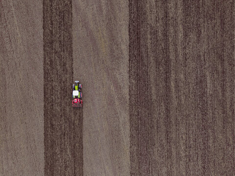 Aerial view of a tractor cultivating dark soil in a vast farmland field in Latvia.