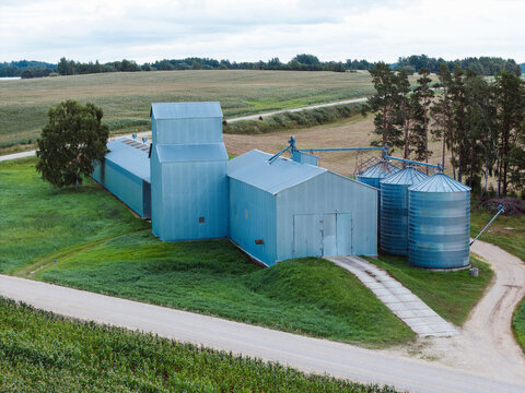Aerial view of grain storage facility with metal silos and a long warehouse building in the rural landscape of Kaive, Tukums Municipality, Latvia.