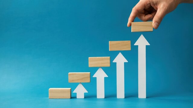 A hand places a wooden block onto an ascending arrow chart on a blue background. Concept of business growth, career development, and corporate success.