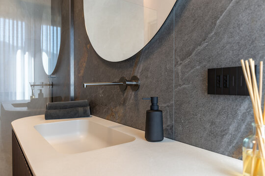 Bathroom vanity accessories photographed with black soap dispenser sitting near center with an amber diffuser, in subdued side daylight.