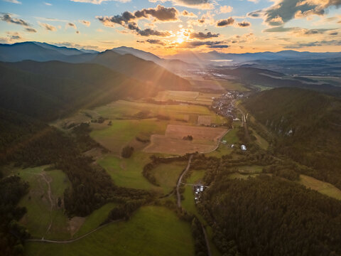 Aerial view of the Valley of Cierny Vah at sunset, featuring lush green fields, rolling hills, and golden light illuminating the landscape in Liptovsky Mikulas, Zilinsky kraj, Slovakia.