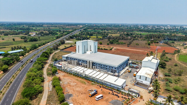 Aerial view of a milk production unit and dairy processing facility with industrial buildings, silos, and parking area surrounded by rural landscape near a highway in Chennai, Tamil Nadu, India.