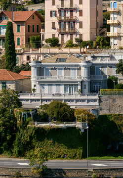 Elegante villa cl&aacute;sica con amplia terraza y balaustrada situada sobre un muro cubierto de enredaderas junto a una carretera costera