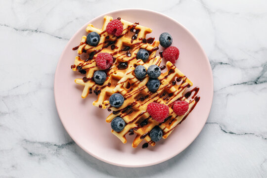 Homemade waffles with chocolate sauce and berries in plate on the table. Top view