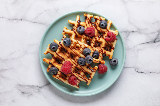 Homemade waffles with chocolate sauce and berries in blue plate on the table. Top view