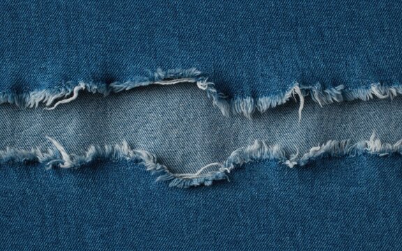 Close-up of ripped blue denim fabric with frayed edges and visible texture