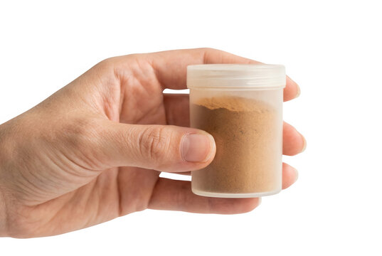 Una mano sosteniendo un peque&ntilde;o frasco de pl&aacute;stico transparente lleno de polvo de color marr&oacute;n, aislado sobre un fondo blanco, ideal para conceptos de ciencia, suplementos o muestras.