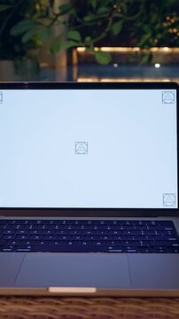Vertical video. Laptop With White Screen Mockup on Wicker Table Near Illuminated Pool at Night, Remote Work Technology and Digital Nomad Lifestyle