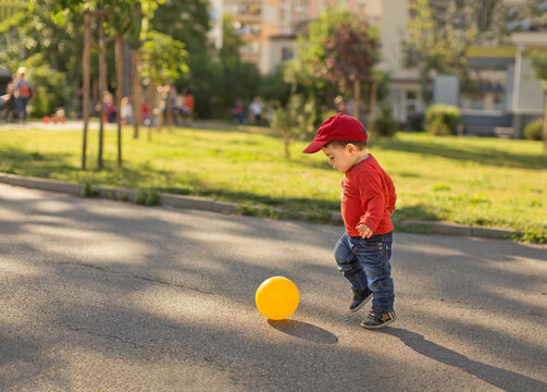 Side view of a young Boy playing football in the street with a yellow ball