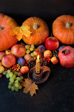 burning golden candle, fruits, autumnal leaves, pumpkins on dark background. festive composition for Thanksgiving or Mabon holidays. organic frech seasonal food, symbol of autumn harvest