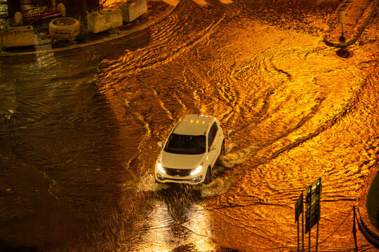 A night-time aerial view of a car driving through the water following a storm in the city