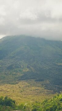 Vertical video. Close View of Gunung Batur Volcano with Clouds Racing Over the Summit During Timelapse Above Rugged Volcanic Terrain