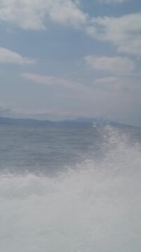 Vertical video. View From Speedboat Racing Across Open Ocean With White Wake Trail and Distant Mountain Coastline Under Dramatic Sky in Slow Motion