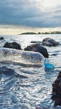Vertical video. Slow Motion Low Angle View of a Plastic Bottle With a Tethered Cap Thrown Into the Sea Above Rocky Shoreline, Ocean Pollution, Marine Waste, Environmental Awareness and Coastal Conserv