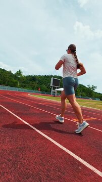 Vertical video. First Person FPV Drone Chasing a Woman Running Around a Stadium Track, Ultra Low Flight, Wide Angle Perspective, Dynamic Fitness Training, Speed and Endurance