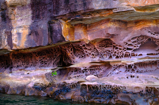 Sandstone formations with erosion patterns along the water in a river setting provide insights into natural processes in Australia