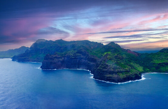Aerial view captures the unique coastline and cliffs of Kauai Island with colorful clouds at sunset in Hawaii