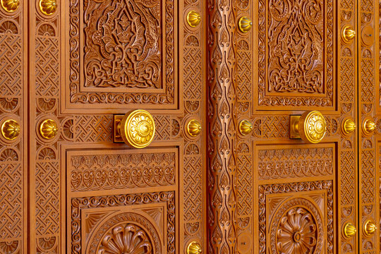 Ornate wooden door with intricate carvings and golden handles at a grand mosque in Muscat