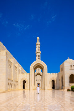 Muslim worshipper walks towards main entrance of Sultan Qaboos Grand Mosque in bright daylight