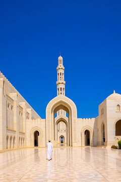 Muslim worshipper walks through the courtyard of Sultan Qaboos Grand Mosque in Muscat Oman under clear blue sky
