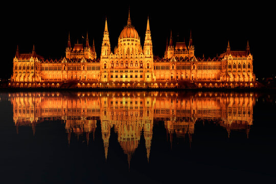 Hungarian parliament building reflects in the Danube River at night with lights illuminating the scene