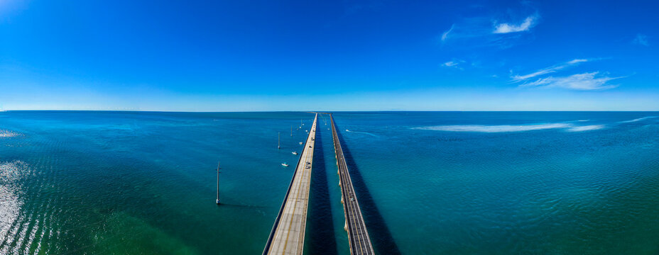 Long bridge stretches over blue waters with minimal boats in the distance and clear skies