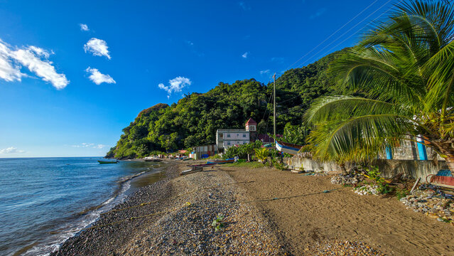 Visitors enjoy time on the shore of Soufriere beach with boats in the water and greenery in the background